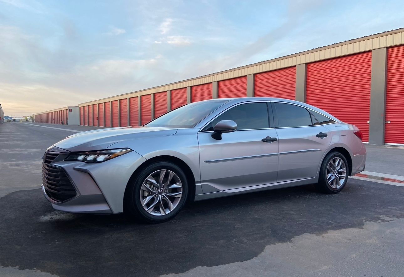 Silver sedan parked in front of red storage units on a clear day.